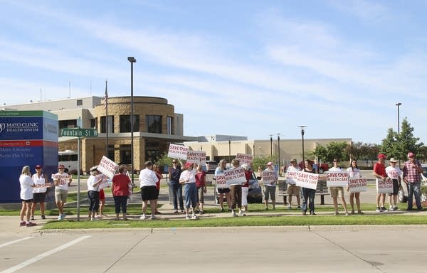 People stand in front of a hospital while holding signs.