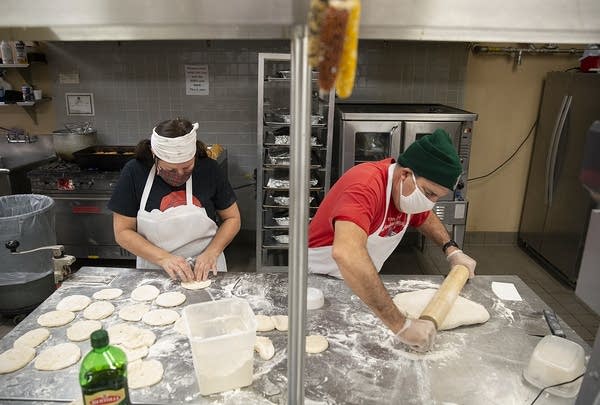 Two people make bread in a commercial kitchen. 