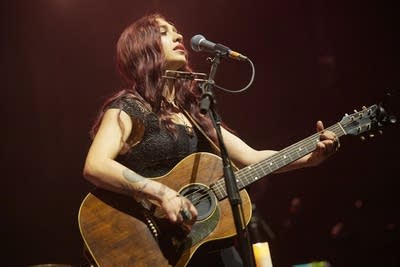 A woman sings and plays guitar onstage in a large music venue
