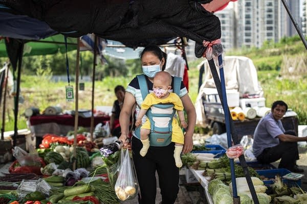 A woman carrying her child buys vegetables at an open market on May 31, 2021 in Wuhan, China.