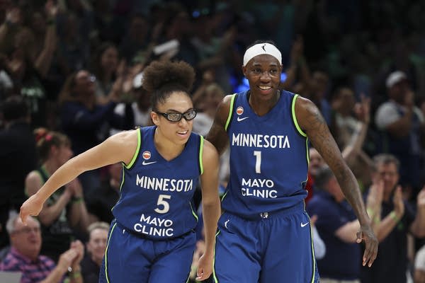 Two WNBA players in blue uniforms jog across the court.