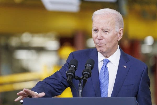 A man in a blue suit stands and talks at a podium