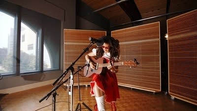 A woman sings and plays guitar in a recording studio