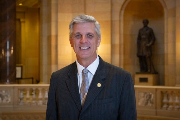 A man poses in the capitol, wearing a suit and tie.