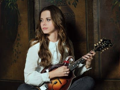 A woman sits on a quilt and plays mandolin