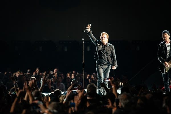 A man waves to an audience from a stage in a large stadium