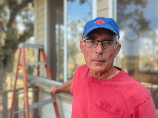 A man in a red shirt leans against a latter