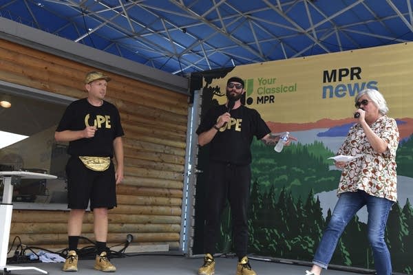 Three people with microphones onstage at a fair