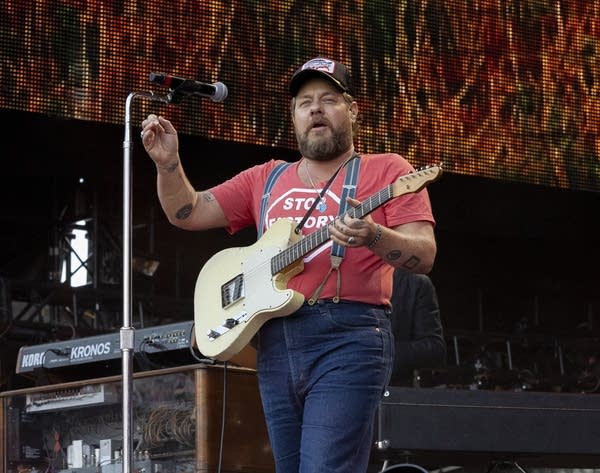 A man sings and plays guitar on a large outdoor stage