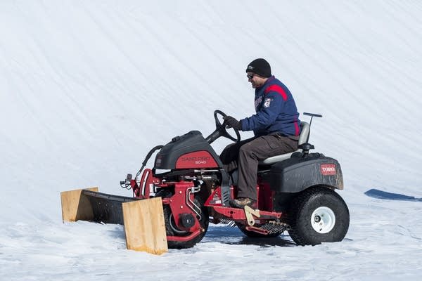 A tractor, normally used to groom the infield dirt, plows ice and a snow