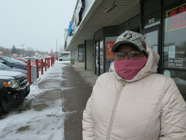 A woman in a mask stands on a sidewalk. 