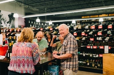 A group of people gather at a table where wine samples are poured