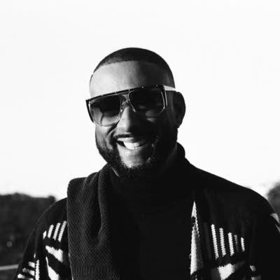 A man in sunglasses and a suit smiles at the camera