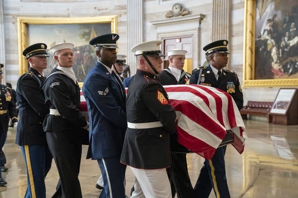 Military members carry a casket draped with the American flag.