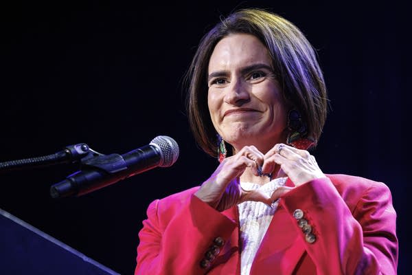 A person smiles and makes a heart symbol