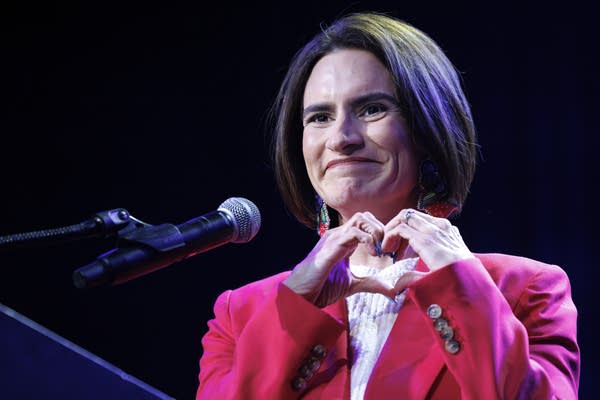 A person smiles and makes a heart symbol