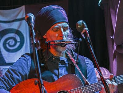 A man plays harmonica and acoustic guitar.