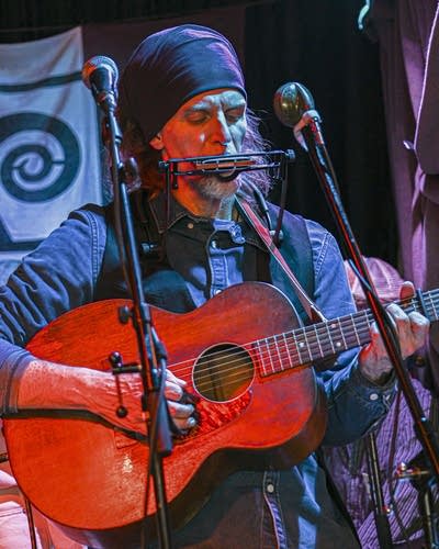 A man plays harmonica and acoustic guitar.