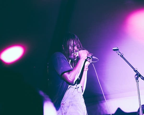 A musician sings into a microphone on a stage inside a large tent