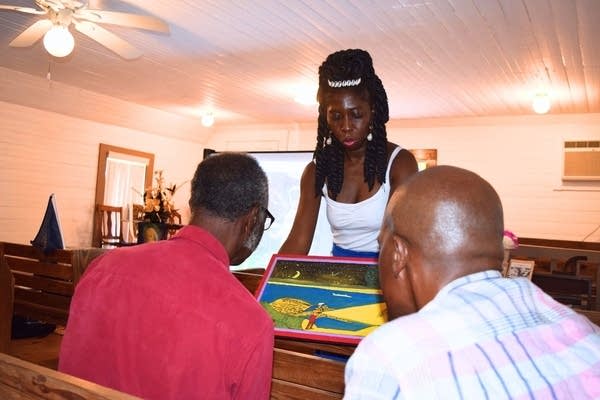 A woman shows two people a work of art.