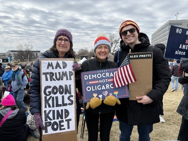 Three people pose for a photo while showing off their protest signs.