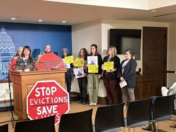 A group stands around a podium and a sign that reads "stop evictions save lives"