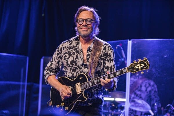 A man smiles and plays guitar onstage