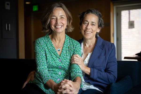 Two women pose for a photo on a couch