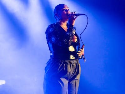 Person holds a microphone in hand while singing under blue lights