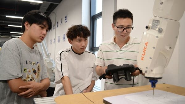 Three students in Nanjing's Zhinanche Robot Technology training school try to program a robotic arm. The manufacturing sector in China needs people who can control and maintain industrial robots.