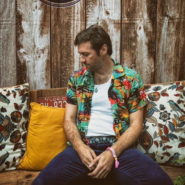A man in a vest and short-sleeve shirt sits on a bench on a patio