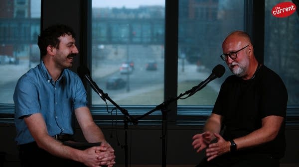 Two men have a conversation in a recording studio
