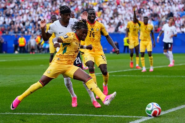 A soccer player in yellow lunges for the ball in front of a player in white.