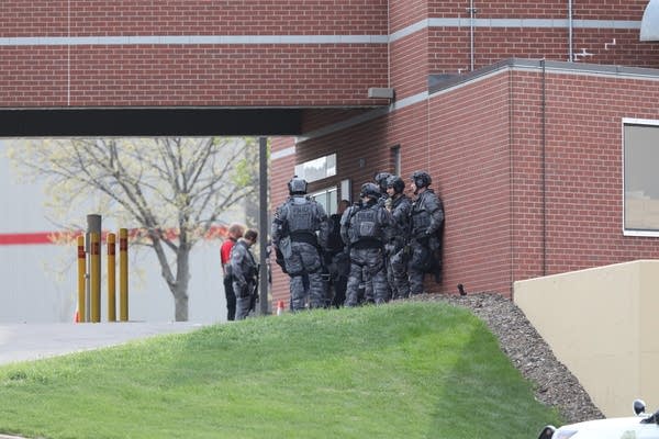 Police in tactical gear stand outside of a bank.