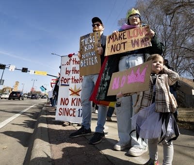 People hold signs while standing on the sidewalk