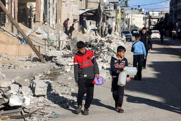 Children walk with plastic fluid containers past the rubble of a building that was destroyed during Israeli bombardment in Rafah in the southern Gaza Strip on February 14, 2024, amid the ongoing conflict between Israel and the Palestinian Hamas militant group.