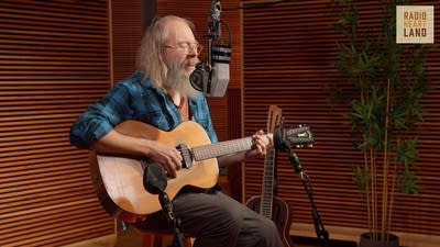A musician sings and plays guitar in a recording studio