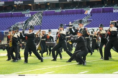 A marching band performs on the field of a football stadium.