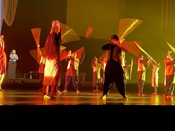 Performers spin a prop on a stage cast with deep orange-yellow light.