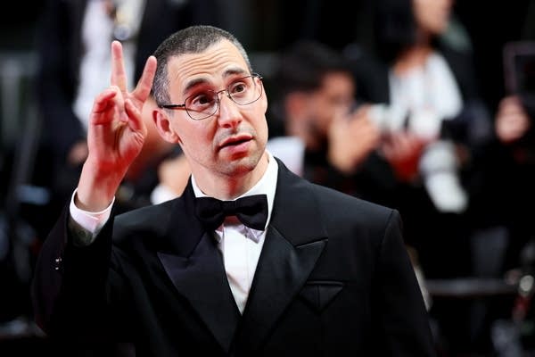 A man in a tuxedo waves to the audience while arriving a film event