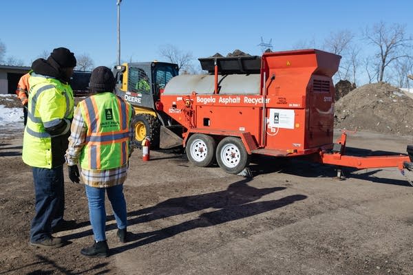 Two people in hi-vis vests look at a large, red machine on wheels.