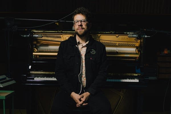 A man sits on a piano bench in front of an open piano