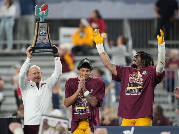 A football coach and players celebrate with a trophy.
