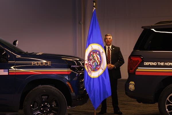 security standing by Minnesota state flag and vehicle