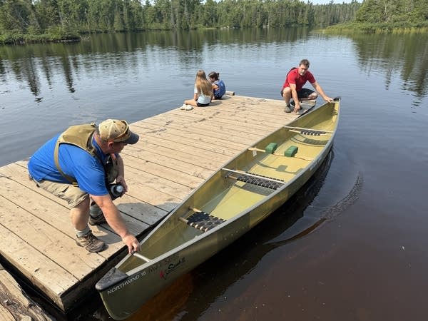 People on a dock prepare a canoe in the water.