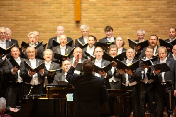 Rows of men dressed in black suits sing during a performance