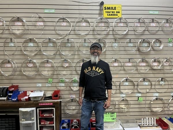 A man stands in front of a display of spools of jewelry materials.