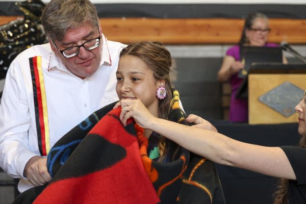 A man helps place a blanket around a student.