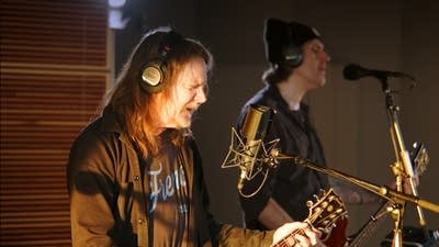 Two musicians sing and play instruments in a recording studio