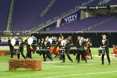 A marching band performs on the field of a football stadium.